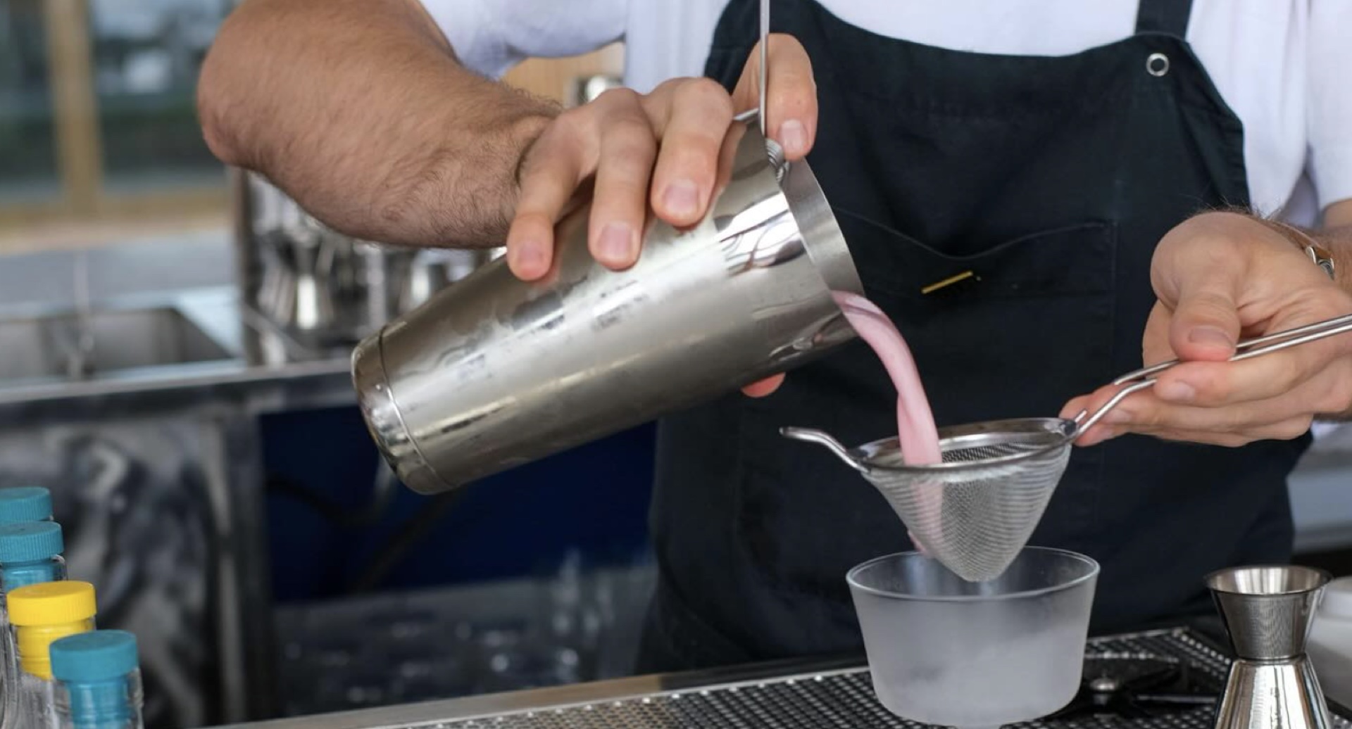 A bartender straining a pink cocktail
